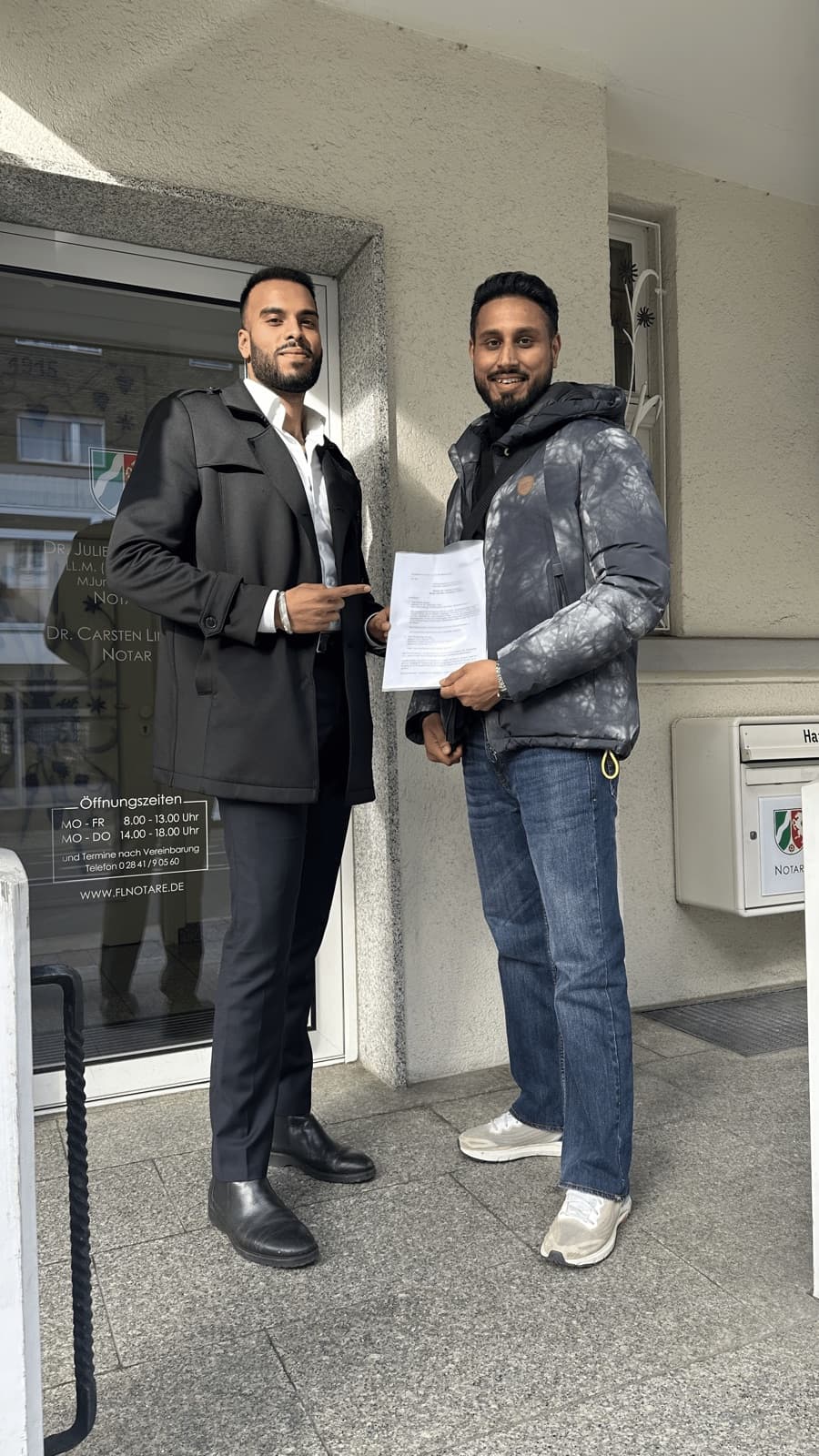 Kunde mit Vertragsunterlagen in der Hand, gemeinsam mit einem Berater vor dem Gebäudeeingang